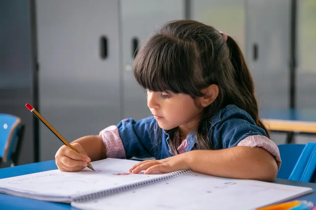 dziewczynka odrabia pracę domową i pisze coś w zeszycie ołówkiem