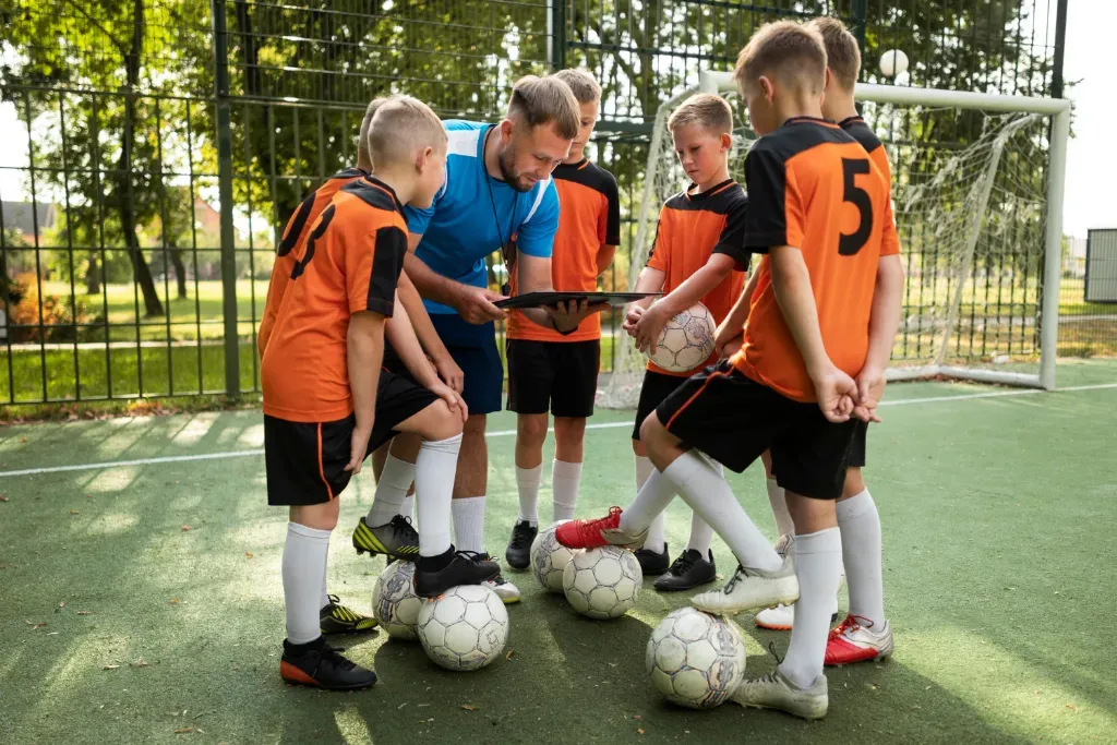 grupa chłopców w stroju piłkarskim rozmawia z trenerem przy bramce