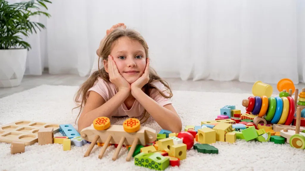 dziewczynka leży na dywanie i bawi się kolorowymi zabawkami